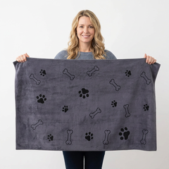 A woman holding up a dark gray pet towel featuring a pattern of black paw prints and bones, set against a plain white background.