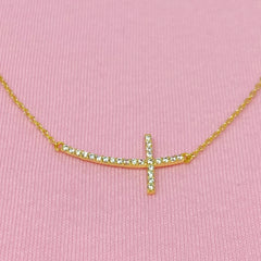 Gold necklace with a cross pendant on a pink background