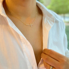 Person wearing a gold necklace with a small pendant, blurred green background